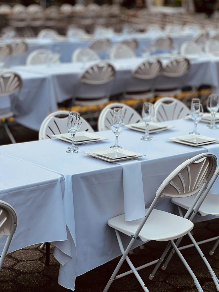 Rows of white tables set for an outdoor event with elegant arrangements.